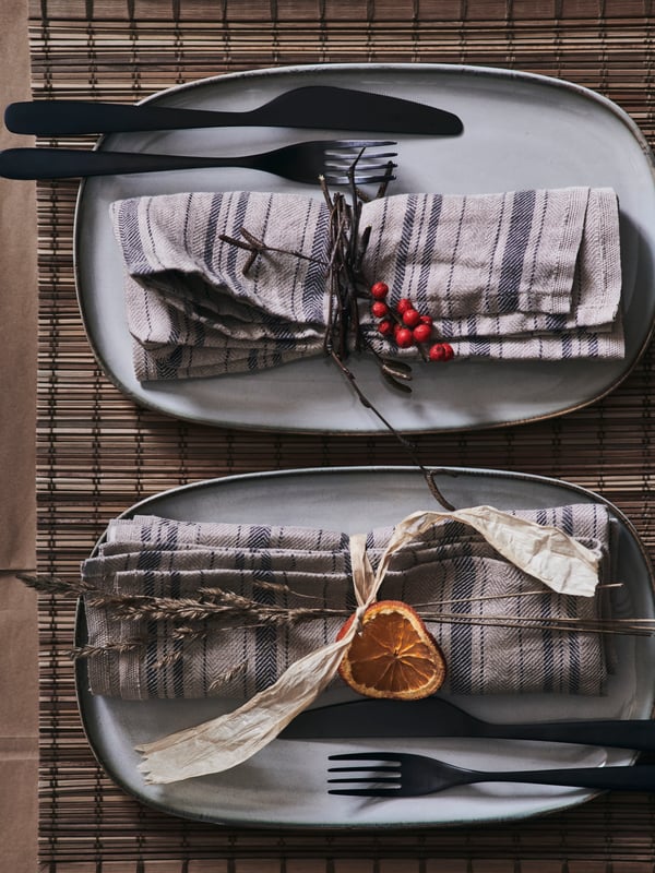 Dresse la table de Noël avec des assiettes GLADELIG décorées avec des serviettes en tissu et des éléments naturels comme des brins d'herbe, des tranches d'orange séchée et des baies.