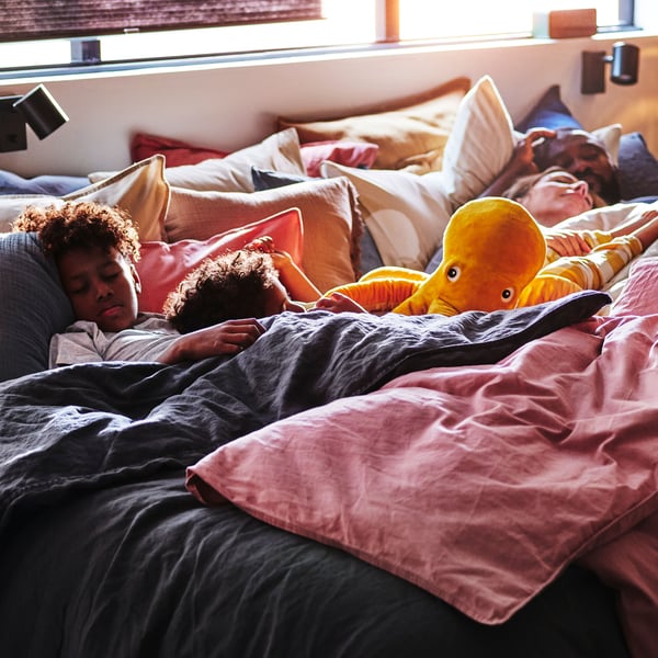 Two children and their parents sleep in a bed with pillows and duvets covered in DYTÅG, ÄNGSLILJA and KLINNETÅG duvet covers.