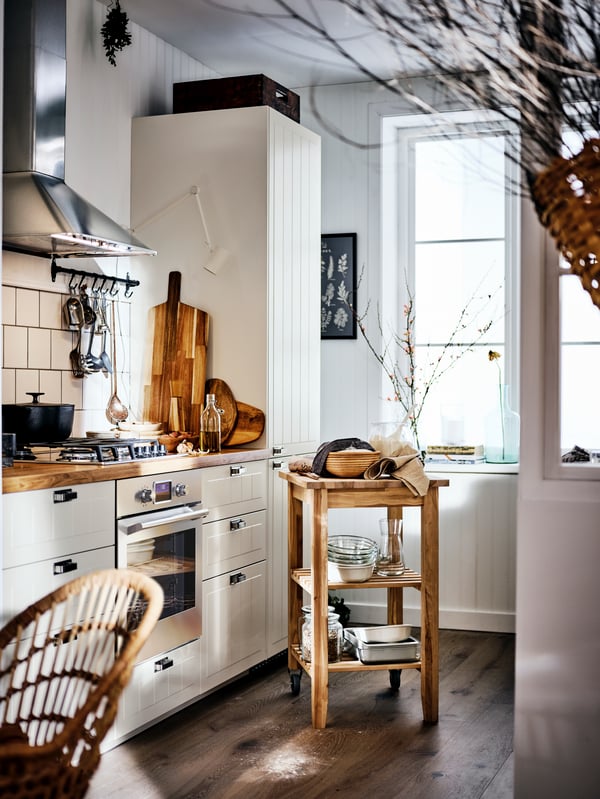 A country-style kitchen with a wooden worktop and beige cabinets, and a BEKVÄM trolley holding bowls and cookware.