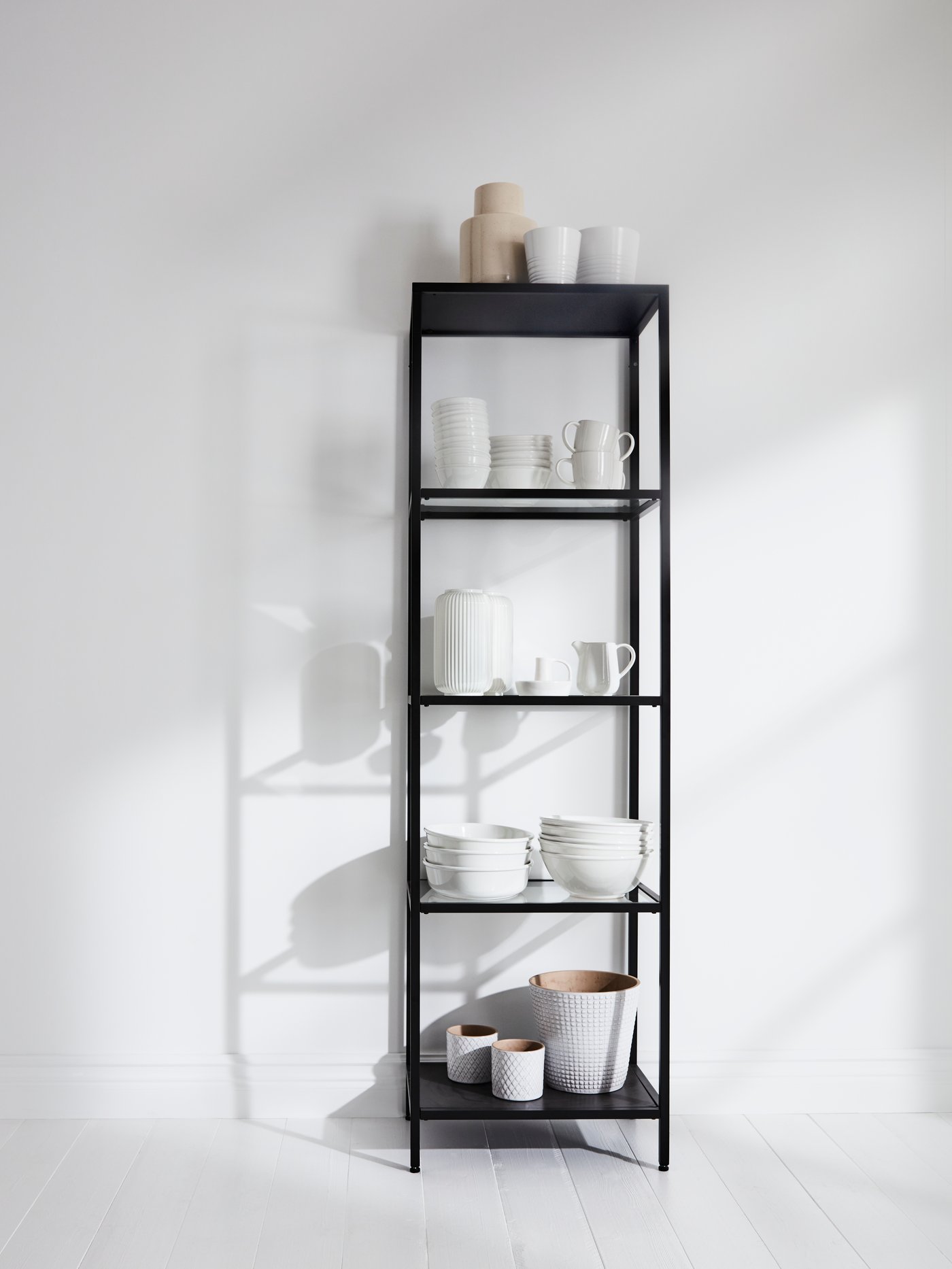 Un estante negro IKEA de 4 repisas con jarrones decorativos y maceteros blancos en sus repisas.