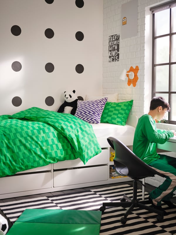 Tween boy at desk in black and white children’s bedroom with bright green check bedding and black and white striped rug.