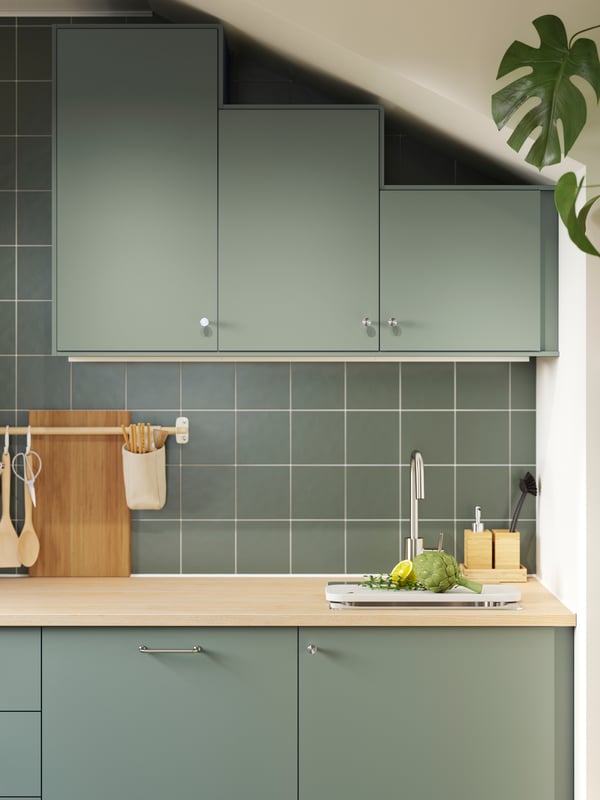 A kitchen with gray green NICKEBO fronts has base cabinets and wall cabinets in various heights following a slanted ceiling.