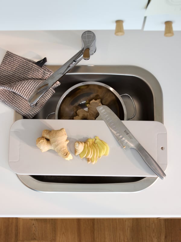 A light grey LILLHAVET chopping board placed over an inset sink on a white/laminate worktop, plus a kitchen mixer tap.