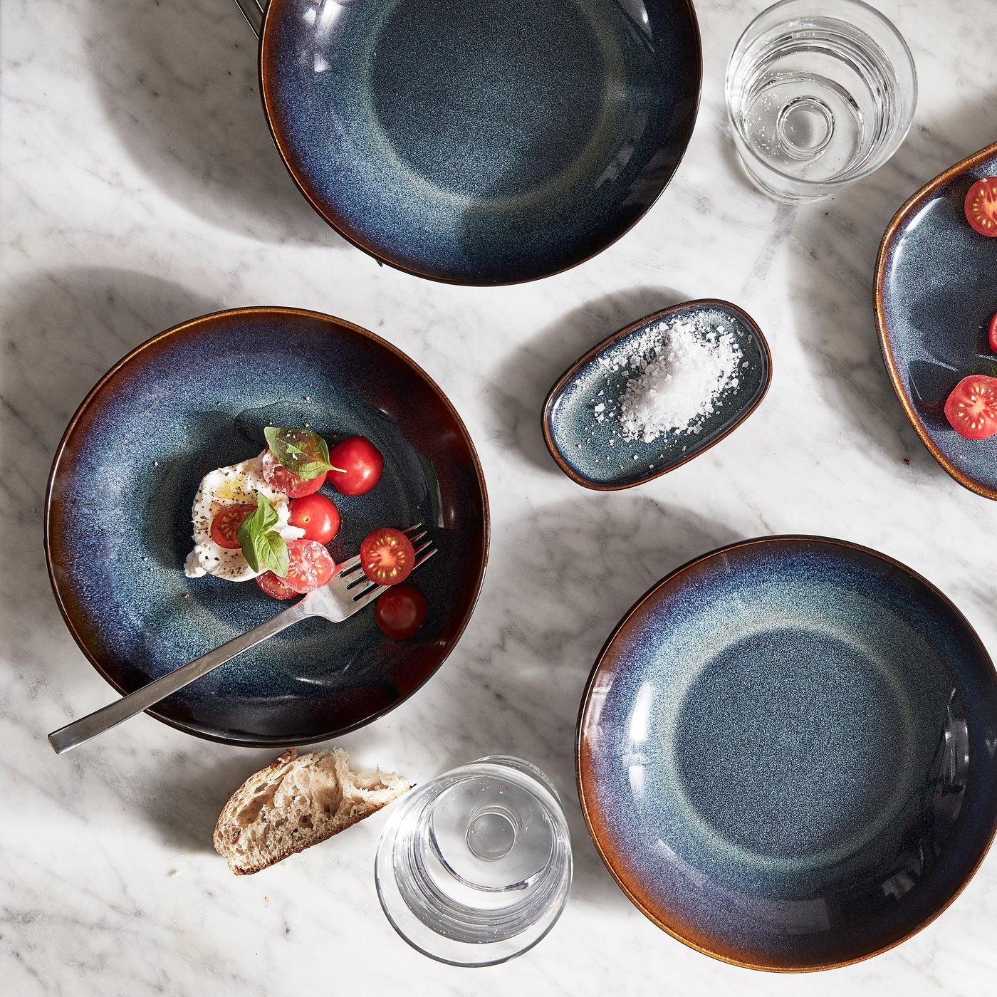 Three IKEA GLADELIG plates in deep blue on a table of white marble finish.