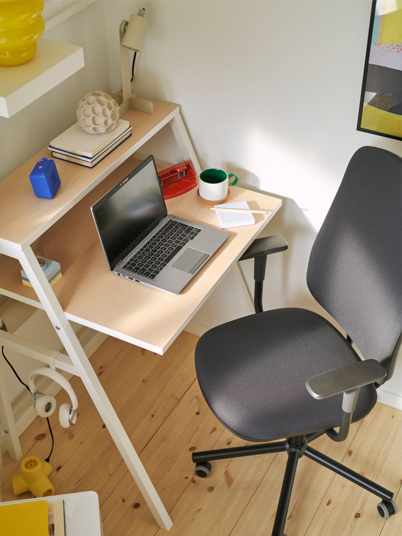 A home office with a dark grey SMÖRKULL office chair with armrests next to a MITTPLAN desk with a laptop and a desk lamp.