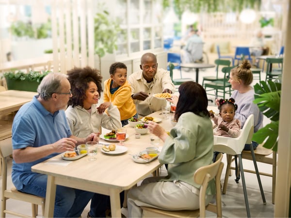 Famille et amis partagent un repas au restaurant IKEA autour d’une grande table avec différents plats et boissons.
