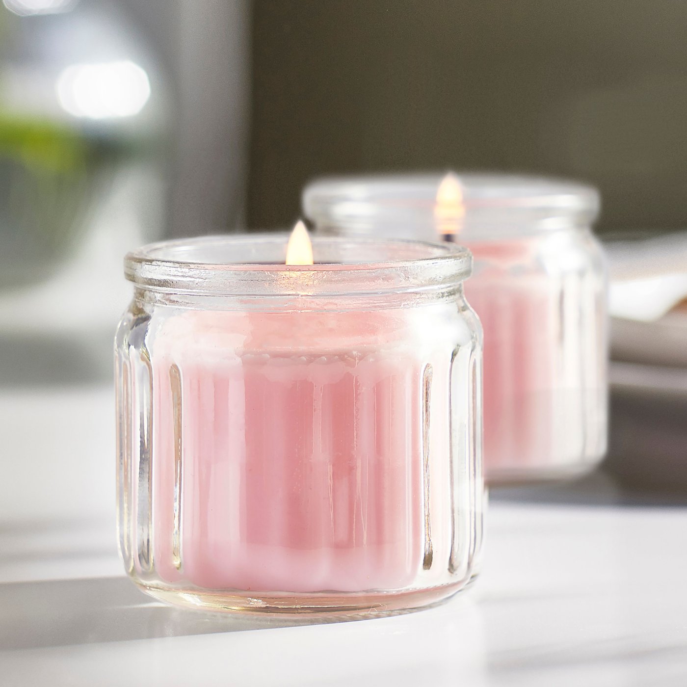 Two pink LUGNARE scented candles on top of white table.