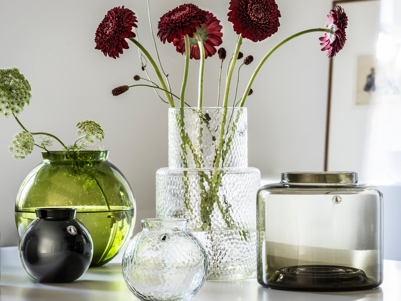 KONSTFULL vases in glass with flowers on a white table in bright room.