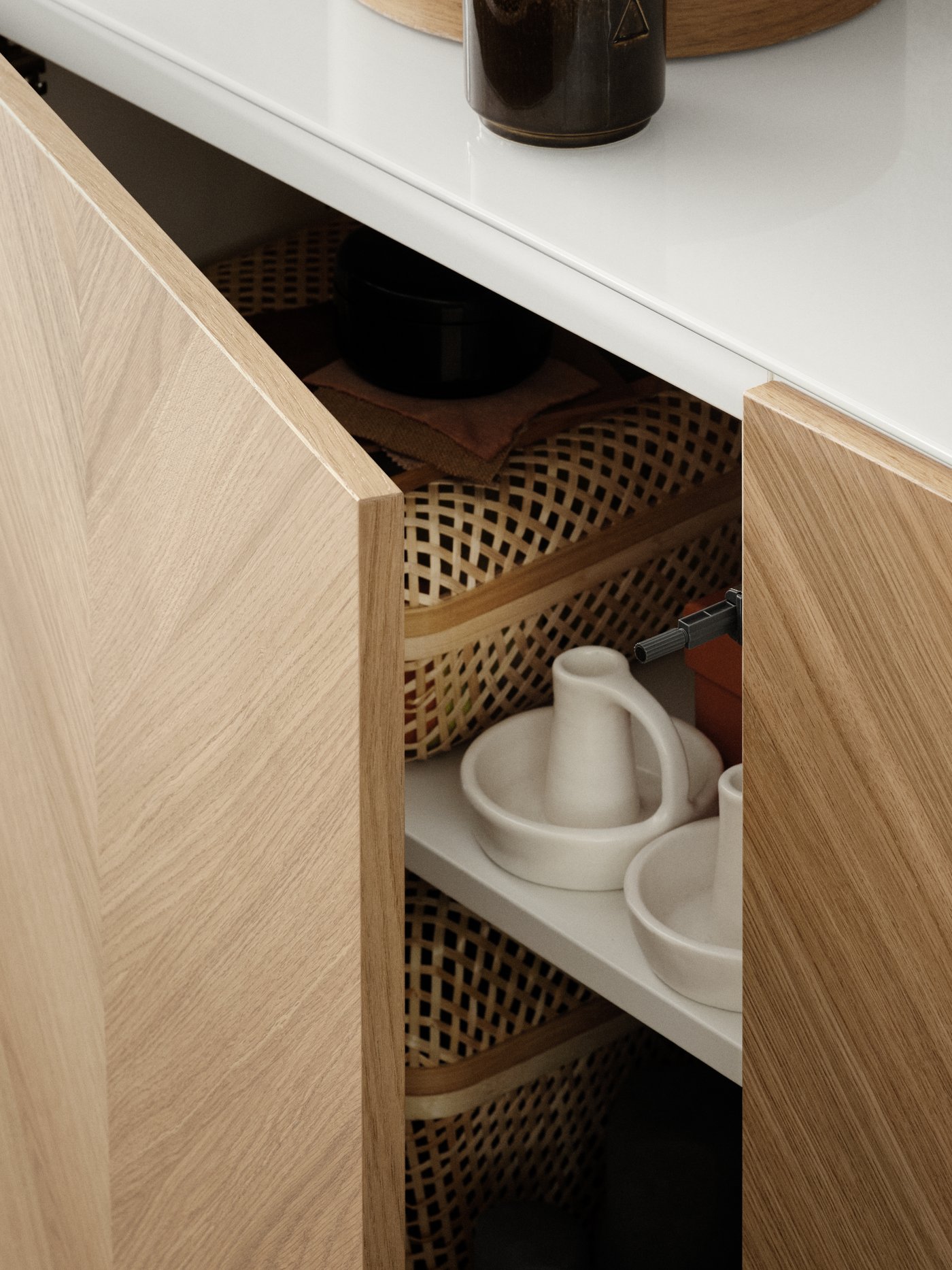 A BESTÅ cabinet with one door slightly open showing candle holders and storage baskets on the shelves.