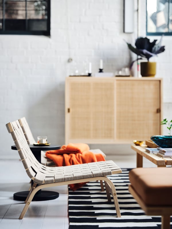Two STOCKHOLM 2025 easy chairs in birch veneer side by side by a coffee table, with a bright orange throw on one of them.