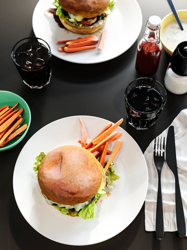 An anthracite table top with plates of burgers, glasses of cola, white napkins, condiments, and cutlery.
