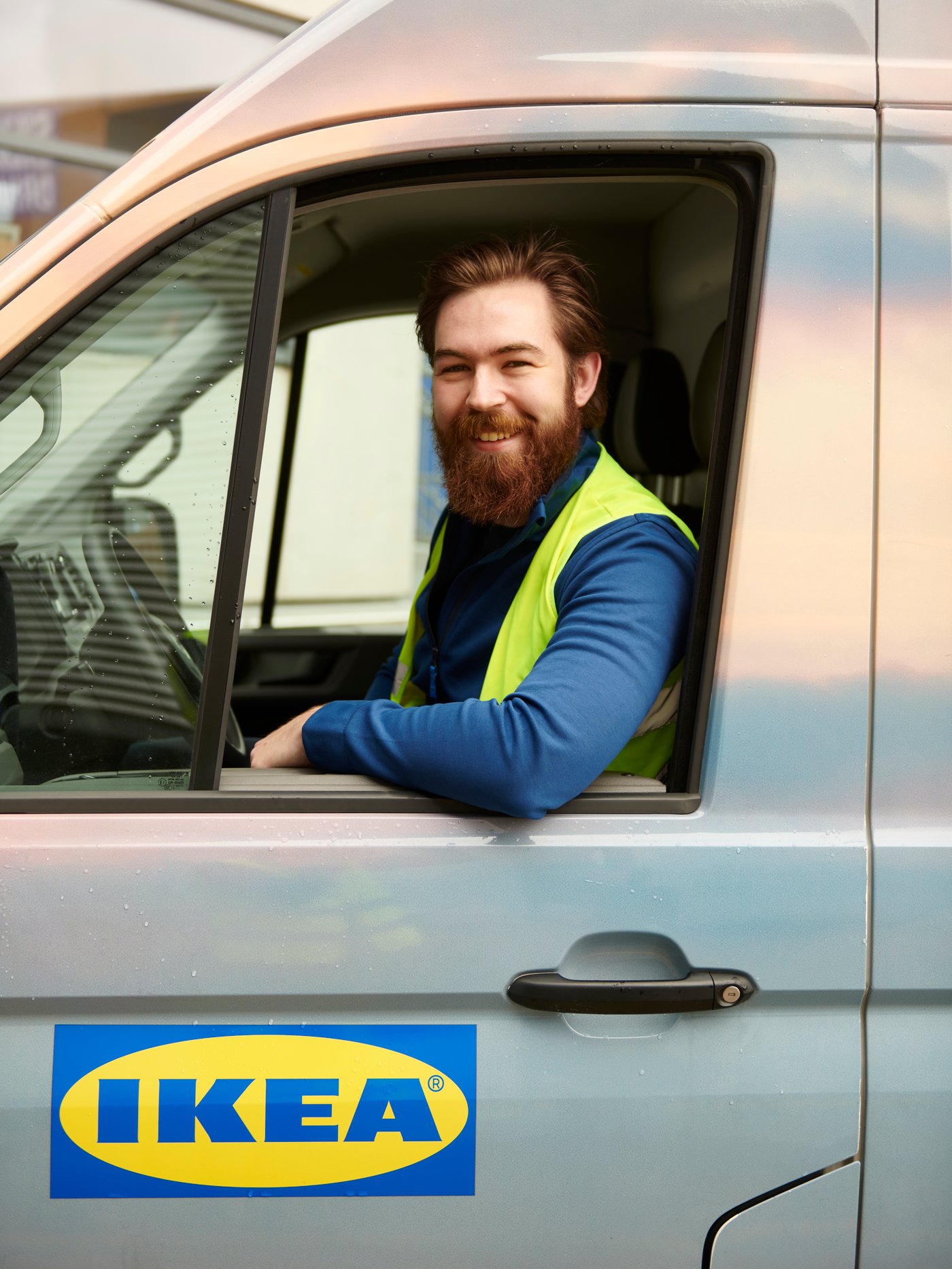 Vozač IKEA kamiona sedi za volanom sa spuštenim prozorom i izbačenim laktom.