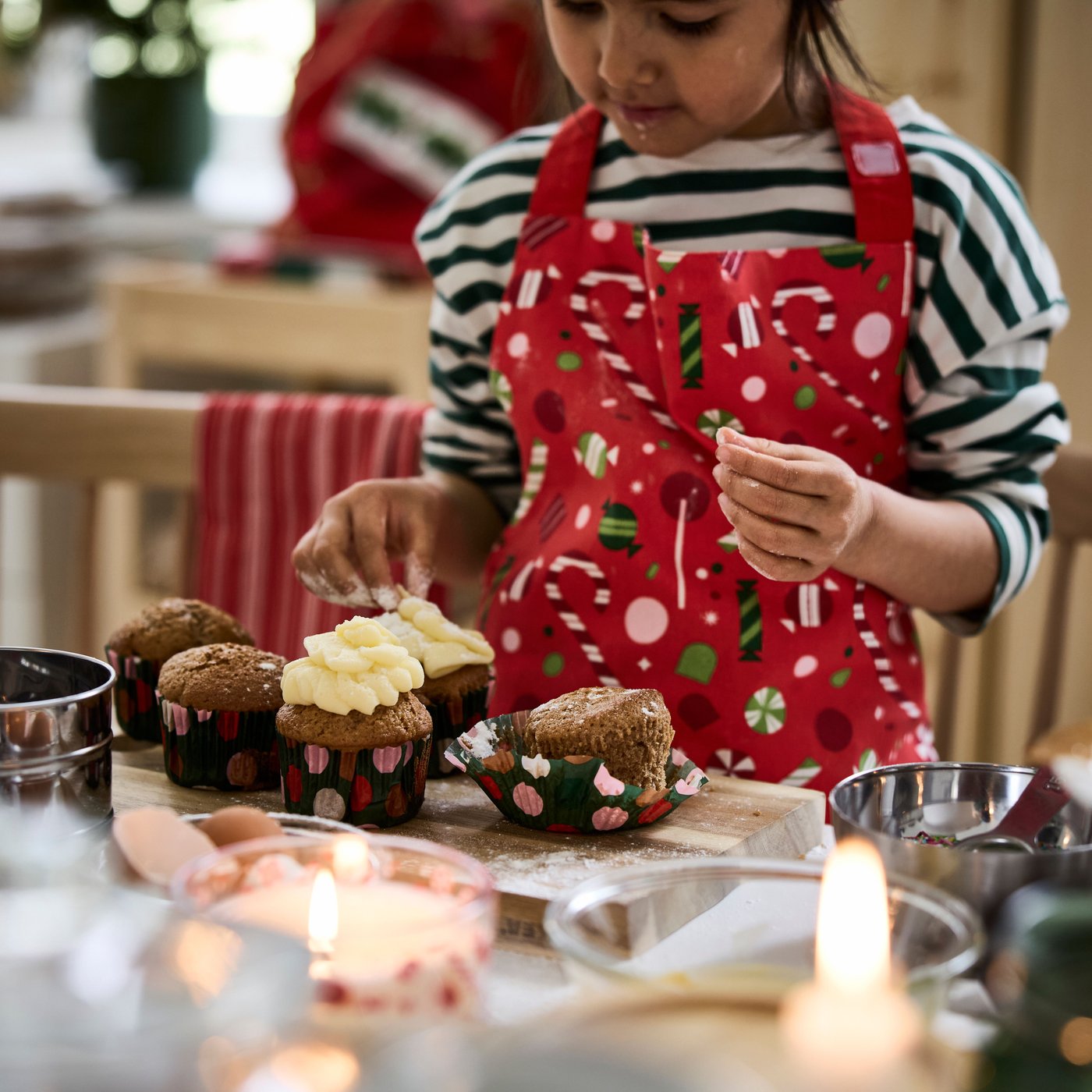 Ein Kind steht mit einer Kinderschürze in der Küche und dekorierte Cupcakes