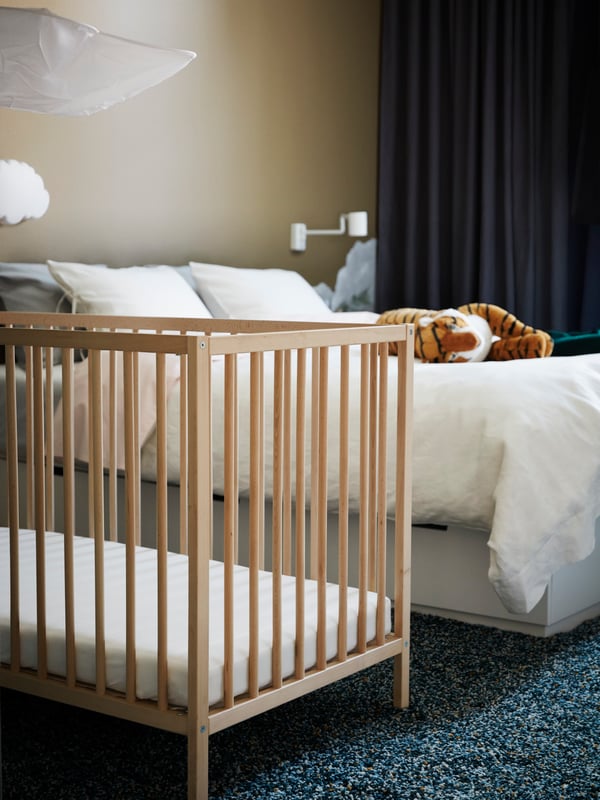 Una cuna SNIGLAR de IKEA al costado de una cama doble en un dormitorio matrimonial.