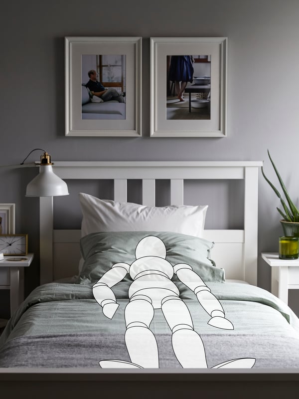 A cartoon drawing of a person lies sleeping on a white HEMNES bed. There are two pictures on the wall above the bed.
