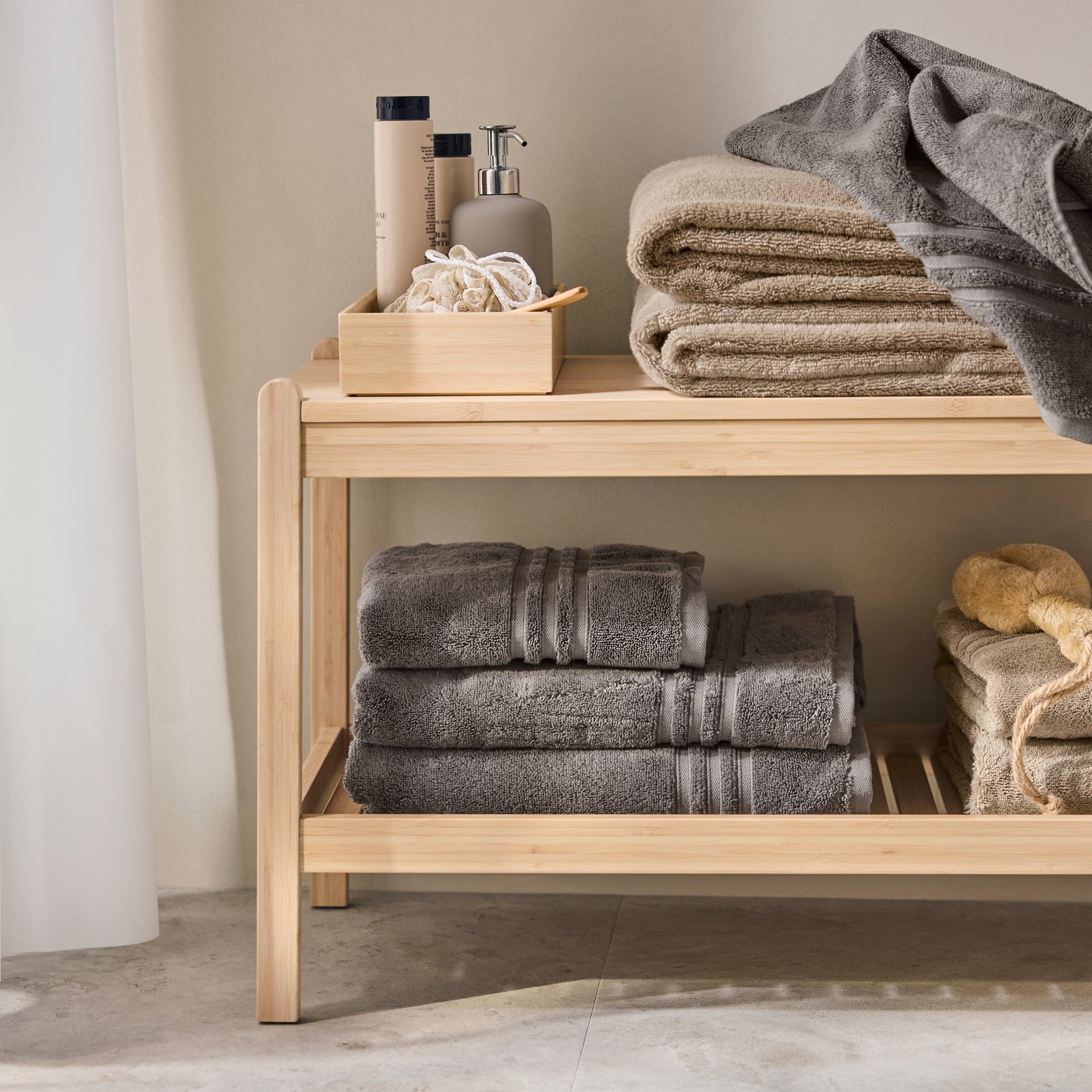 A bathroom with a light wooden shelf displaying neatly stacked grey BROKGLIM bath towels, along with toiletries.