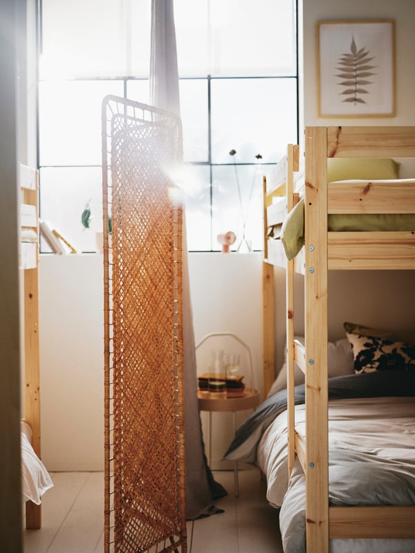 A bedroom with two pine MYDAL bunk beds separated by a handmade rattan TOLKNING room divider and DYTÅG curtains.