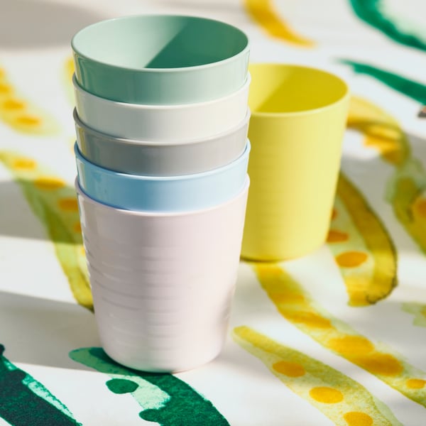 A stack of five coloured, plastic cups sits in front of a yellow cup. A yellow and green patterned tablecloth is underneath.