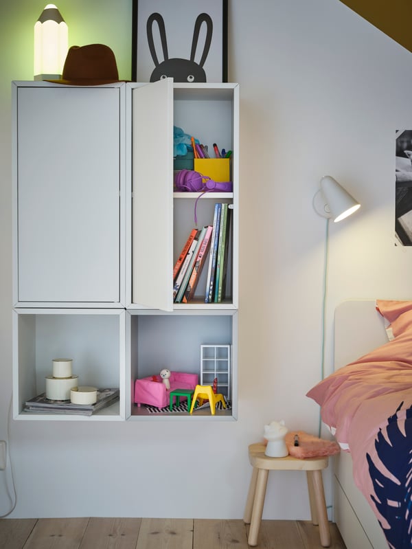 Wall-mounted EKET cabinets with and without doors create a uniform storage solution filled with books and toys.