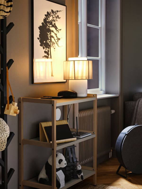 An EKENABBEN open shelving unit against a wall holding devices, chargers and a lamp, with a STARKVIND air purifier nearby.