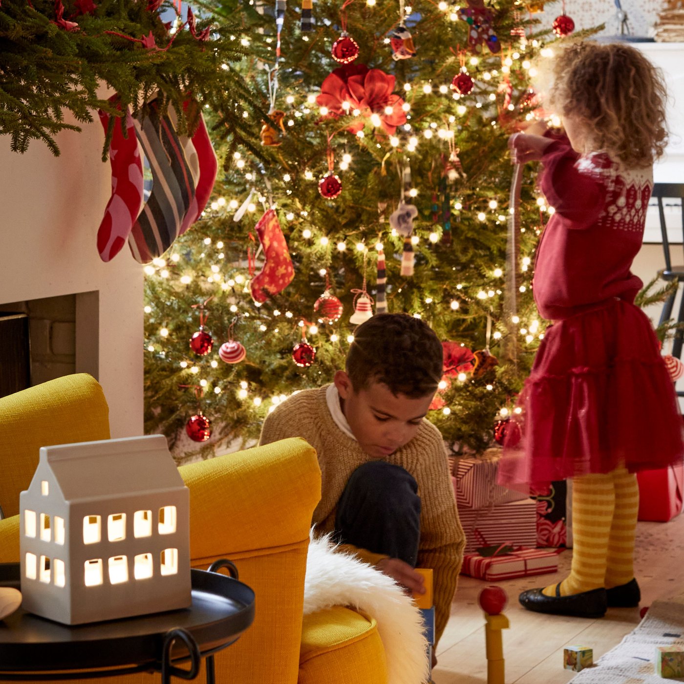 Children decorating a Christmas tree beside a house-themed Scandinavian traditional STRÅLA LED table decoration.