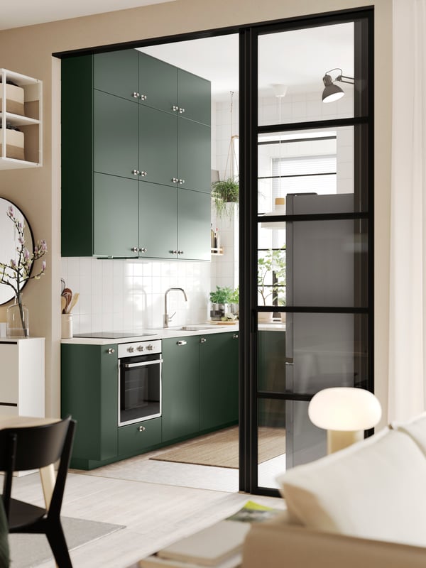 A wide doorway into a kitchen with deep green HAVSTORP kitchen fronts and a white marble effect/laminate EKBACKEN worktop.