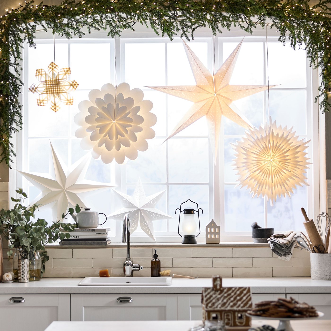 View of kitchen window at Christmas decorated with STRÅLA decorative lighting including star and flower shaped pendants.