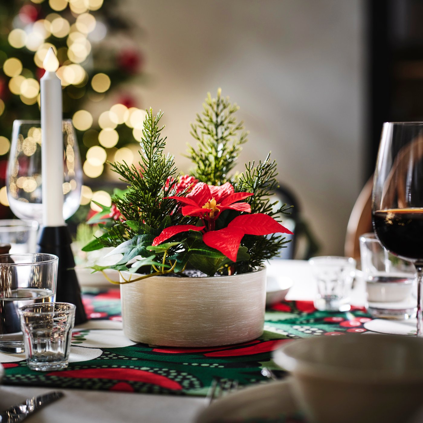 A VINTERFINT plant arrangement with a red poinsettia in a flower pot on a set dining table.