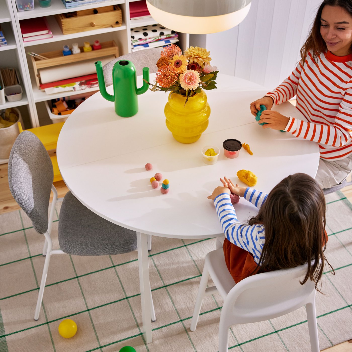 A child plays with colourful toys at a white VIHALS table, surrounded by a vase of flowers and a bright, inviting atmosphere.