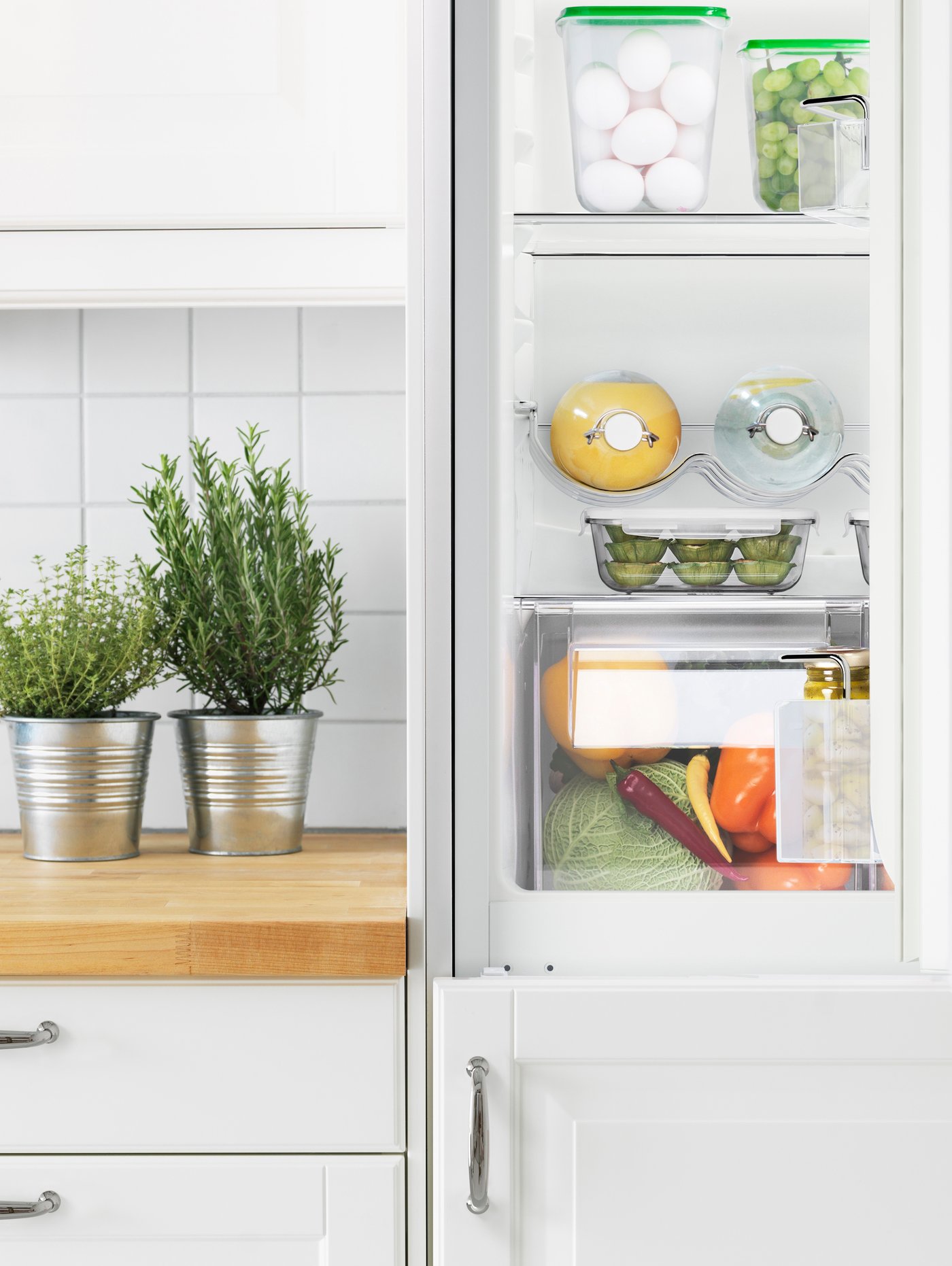 An integrated fridge-freezer half open showing the internal organisation, in a white bright kitchen