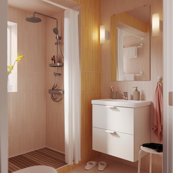 A bathroom in yellow and pink tones, a white bathroom vanity and a LETTAN mirror hanging above. 