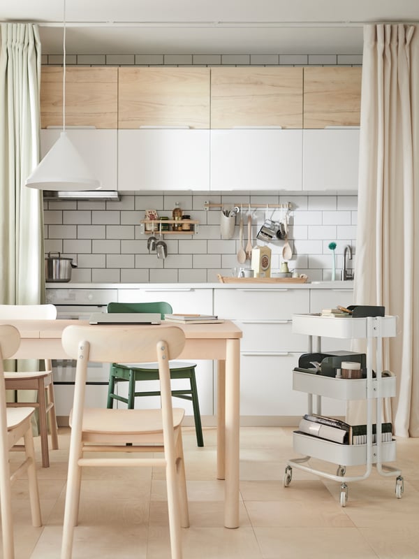 A wooden and white kitchen with wooden tables, chair, and a white cart.