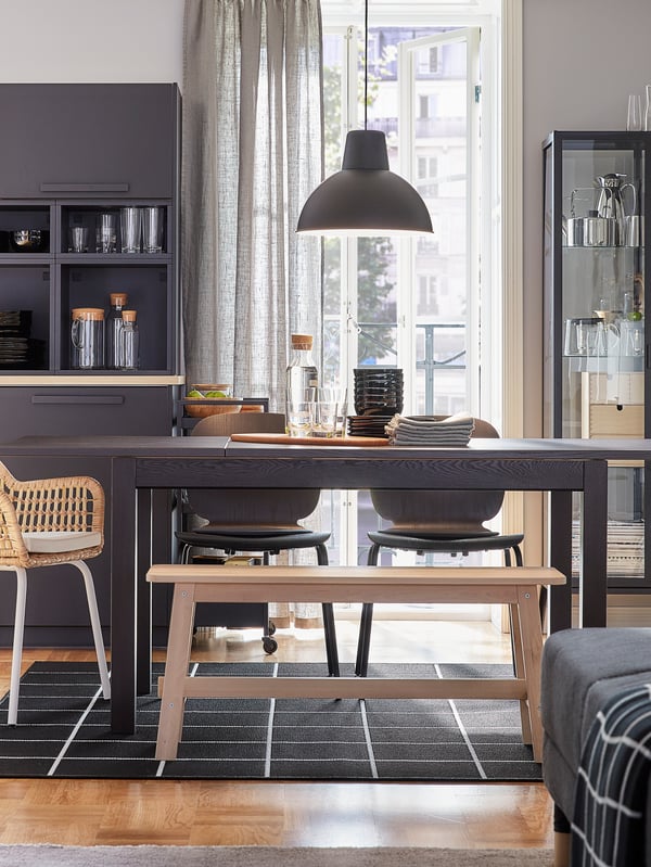 A dining room with an extendable table that’s extended. Black chairs, a rattan chair and a bench in birch provide seating.