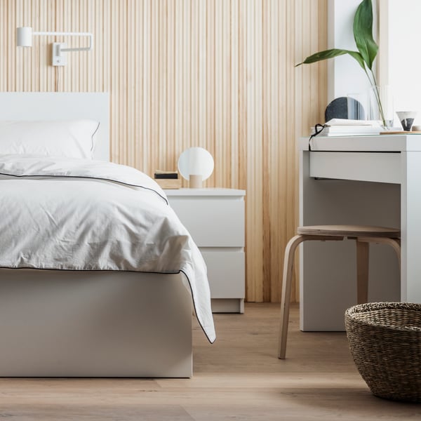A white MALM bed covered in white bed linen in a natural coloured room with a MALM dressing table and birch stool beside it.