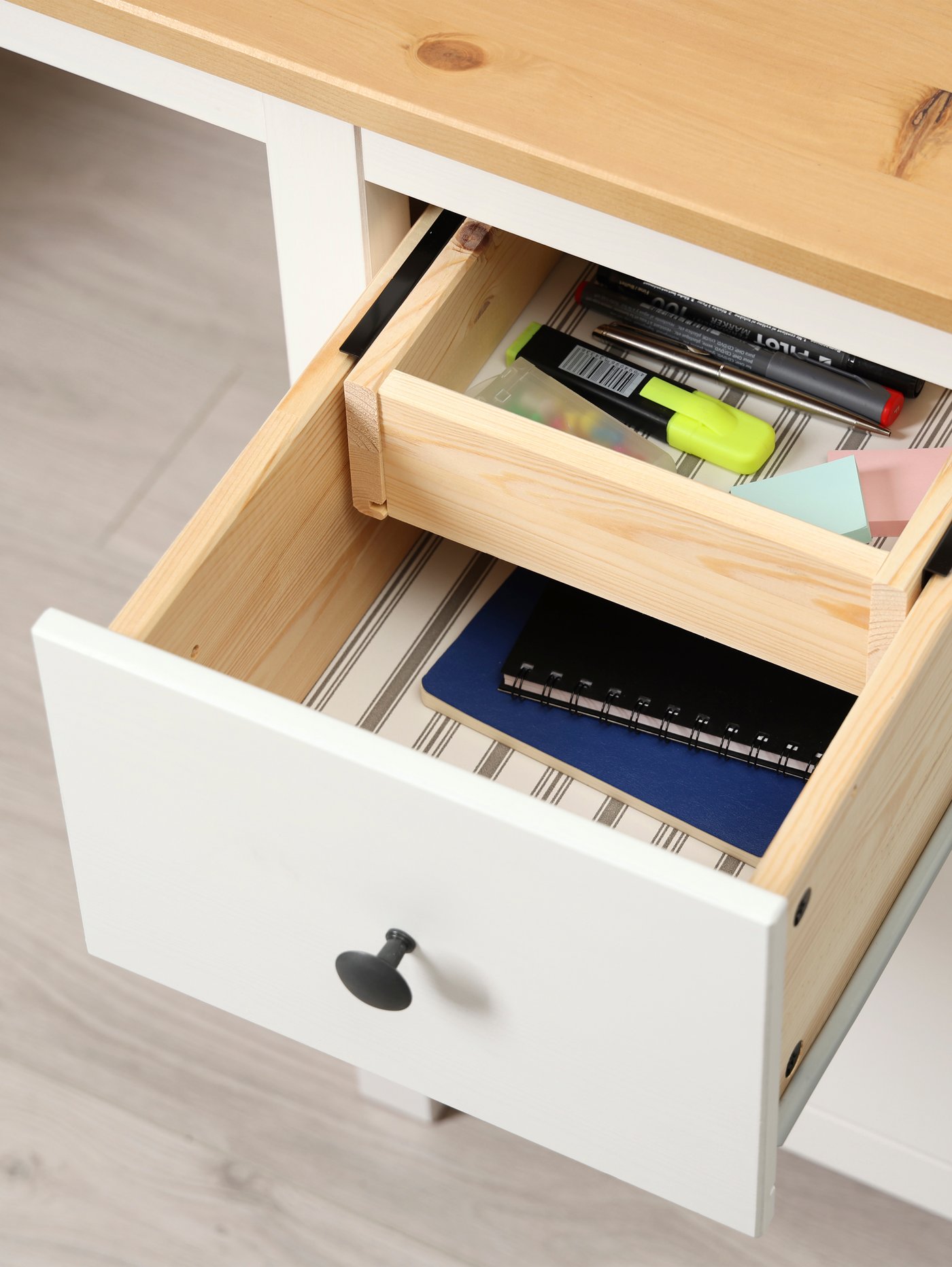 Sebahagian daripada meja HEMNES berwarna putih dan coklat muda dengan salah satu lacinya terbuka, mendedahkan petak kayu di dalamnya.
