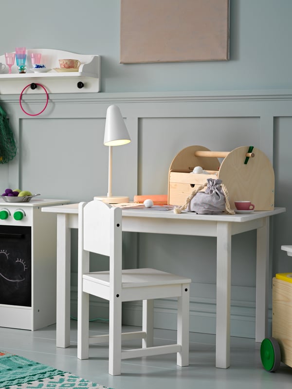 A SUNDVIK children’s chair and a SUNDVIK children’s table with a FUBBLA LED work lamp on top stand in a child’s room.