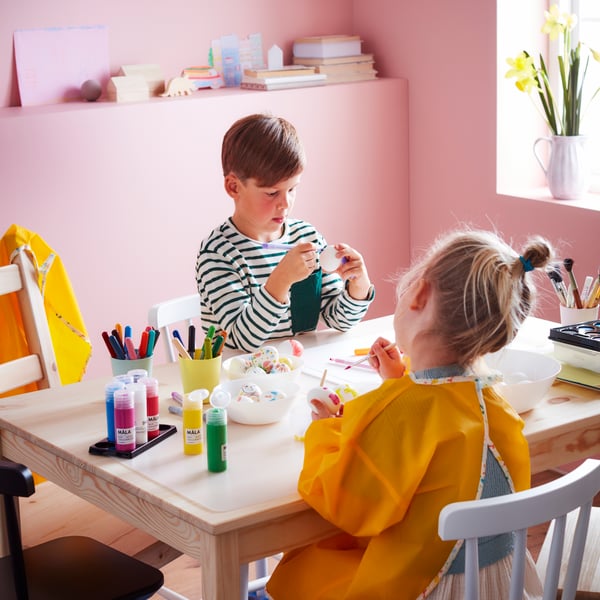Deux enfants sont assis à une table et font des activités manuelles dans une pièce colorée.