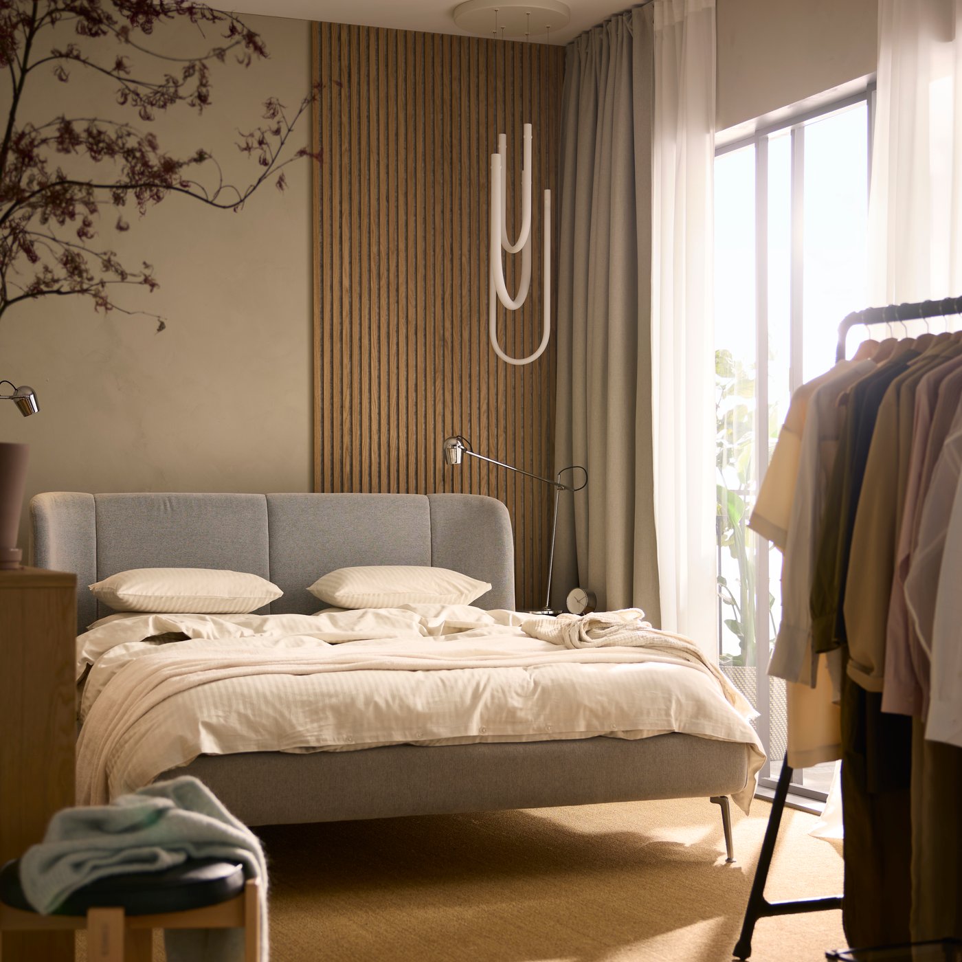A Tallmyra white/black TUFJORD upholstered bed covered in light beige NATTJASMIN bed linen. A VARMBLIXT LED lamp is above it.