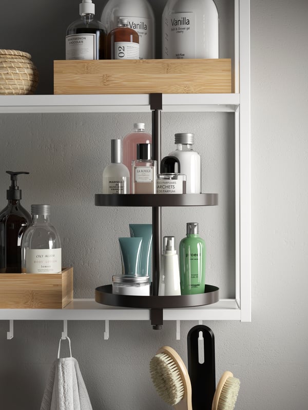 A white shelving unit with a black swivel shelf and bamboo boxes holding beauty essentials. The shelf has hooks underneath.