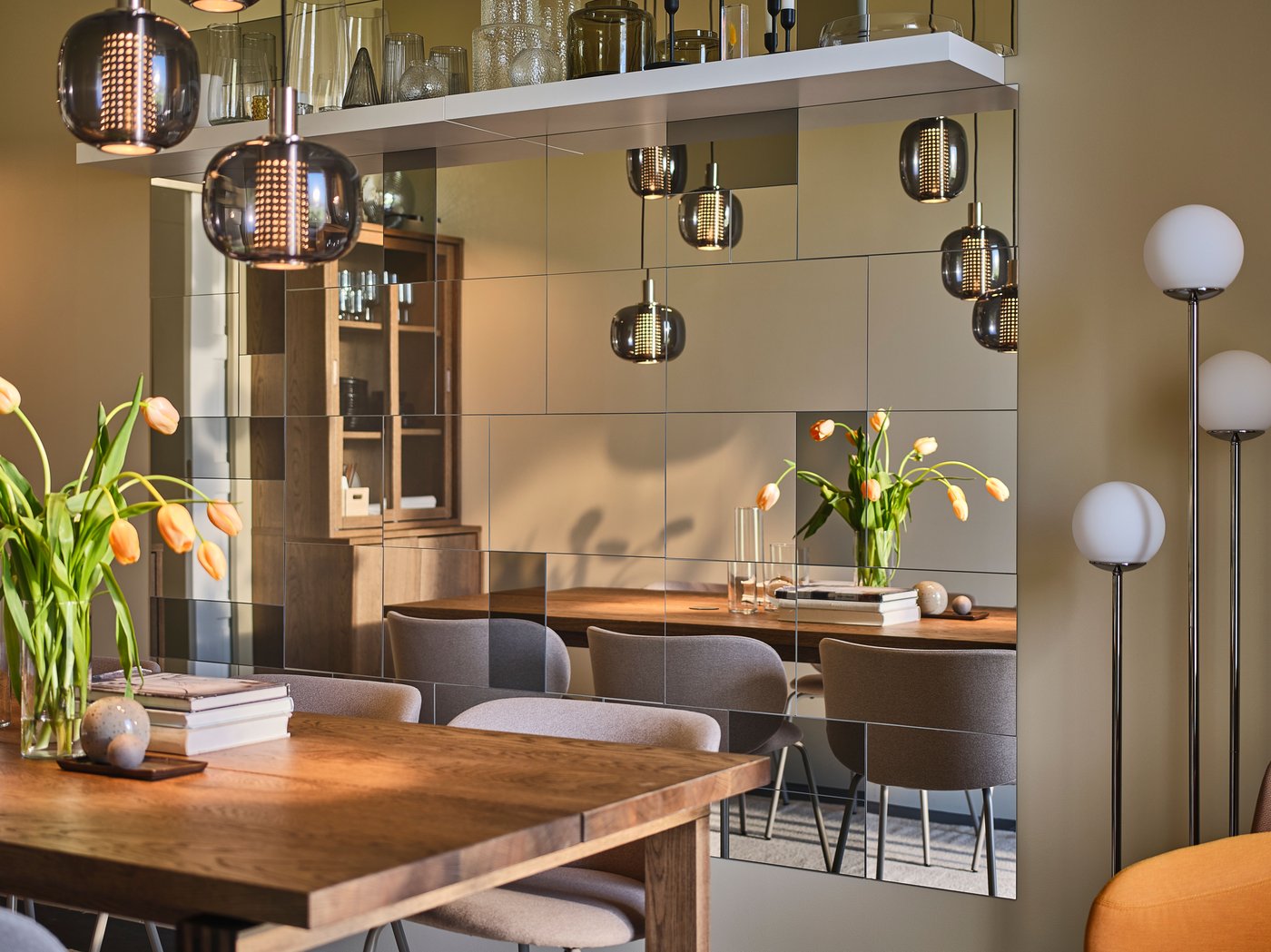 A large MÖRBYLÅNGA table sits in the center of a narrow yet sophisticated dining room with plenty of mirrors on one wall.