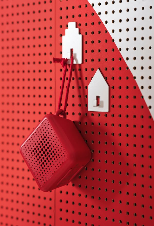 Rdeč Bluetooth zvočnik visi na rdeči vrvici pred belo-rdečo steno.