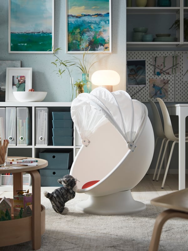 Un fauteuil pivotant blanc/rouge, un chat en peluche gris/blanc, une table basse avec des jouets, des peintures sur le mur.