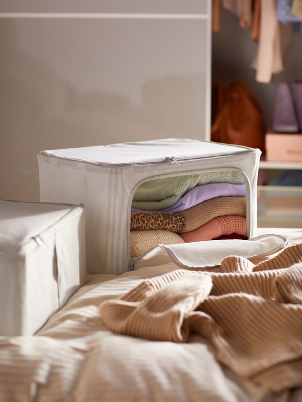 A HEMMAFIXARE storage case with a zip is filled with folded clothes and placed on a bed.