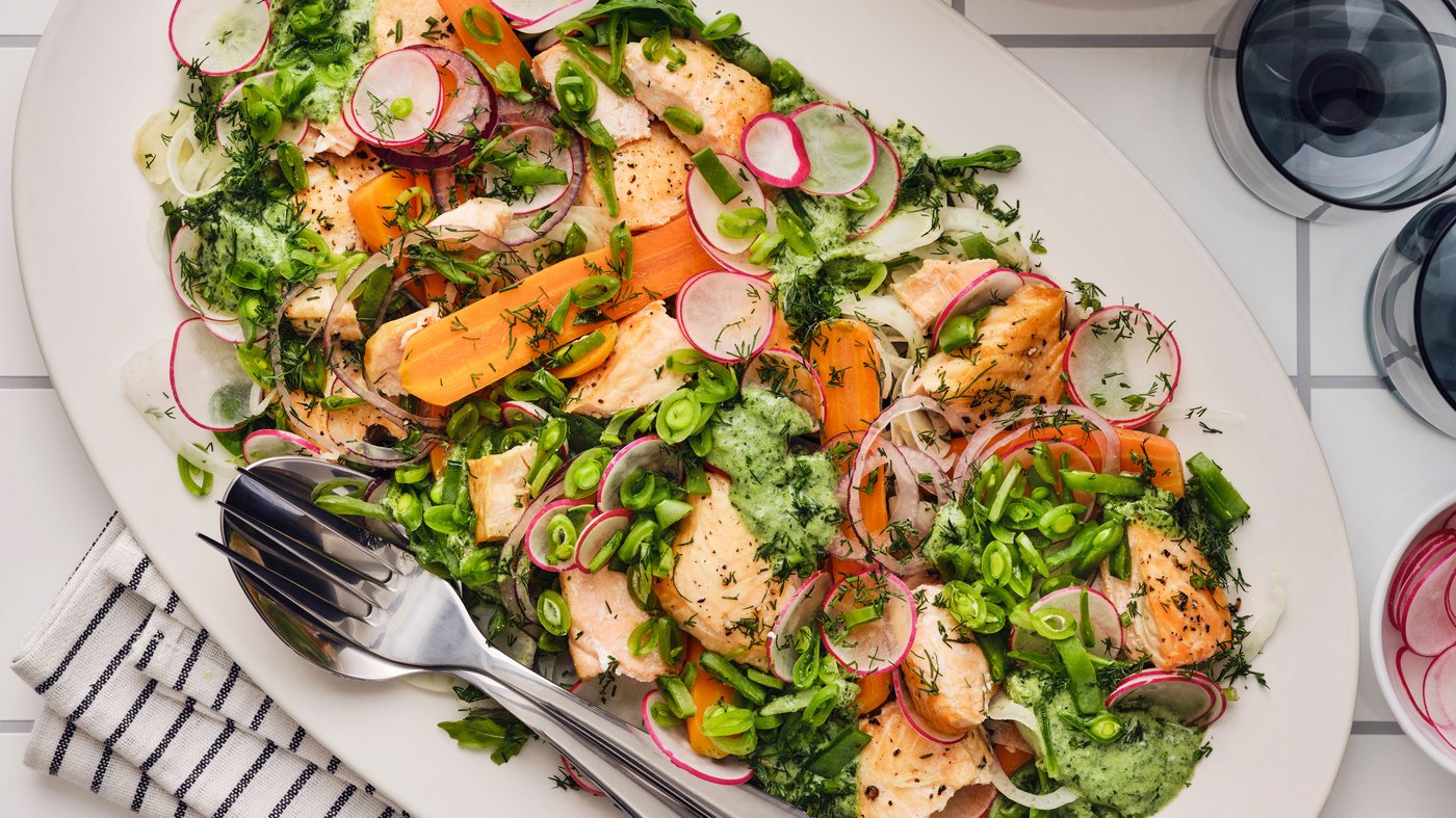 Es ist ein bunter Salat mit gegrilltem Lachs, Radieschen, Karotten, Zuckerschoten und frischen Kräutern zu sehen, der auf einem weißen Teller serviert wird.