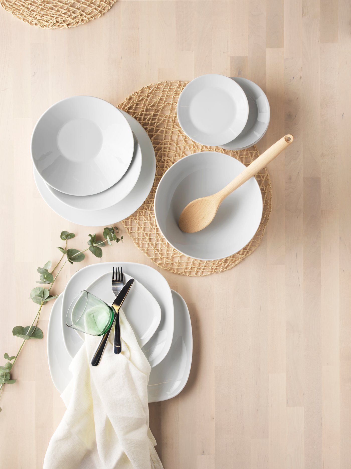 A bird's eye view of IKEA 365+ dinnerware series made of white plates and bowls on top of a wooden dining table.
