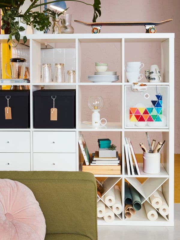 A living room with a white KALLAX shelving unit filled with tableware, art accessories and DRÖNJÖNS and NIMM storage boxes.
