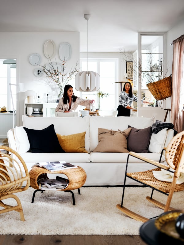 A white BACKSÄLEN sofa and two armchairs in a bright country-style living area with two women at the back of the room.