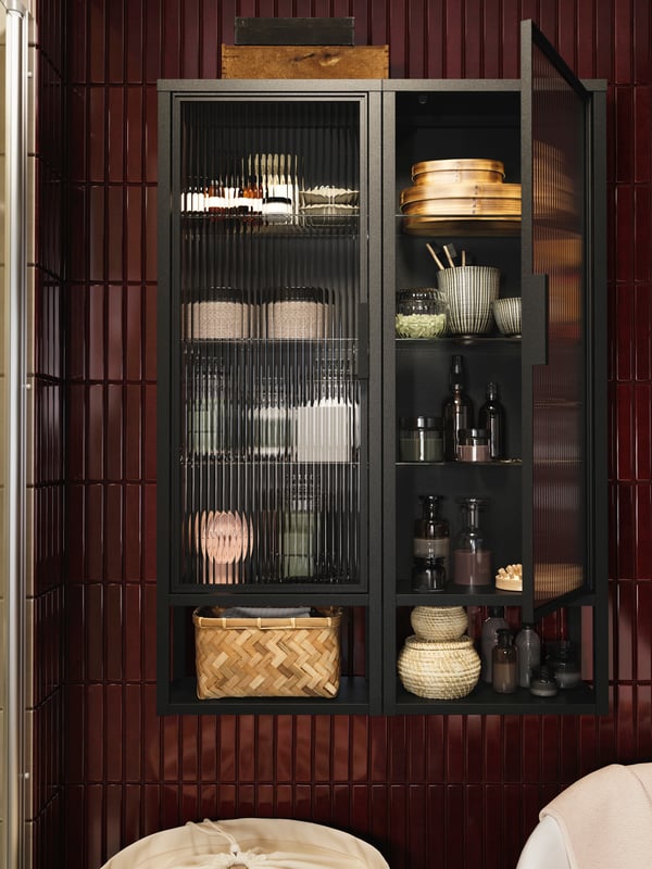 A MOSSJÖN wall cabinet with shelves and glass doors, displaying neatly arranged towels, baskets, and essentials.