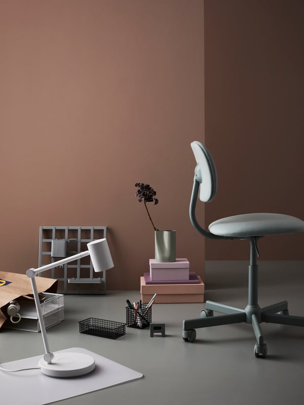 Desk products sit on the floor. PLUGGLAND wire baskets sit near a BLECKBERGET swivel chair. A NYMÅNE lamp is nearby.