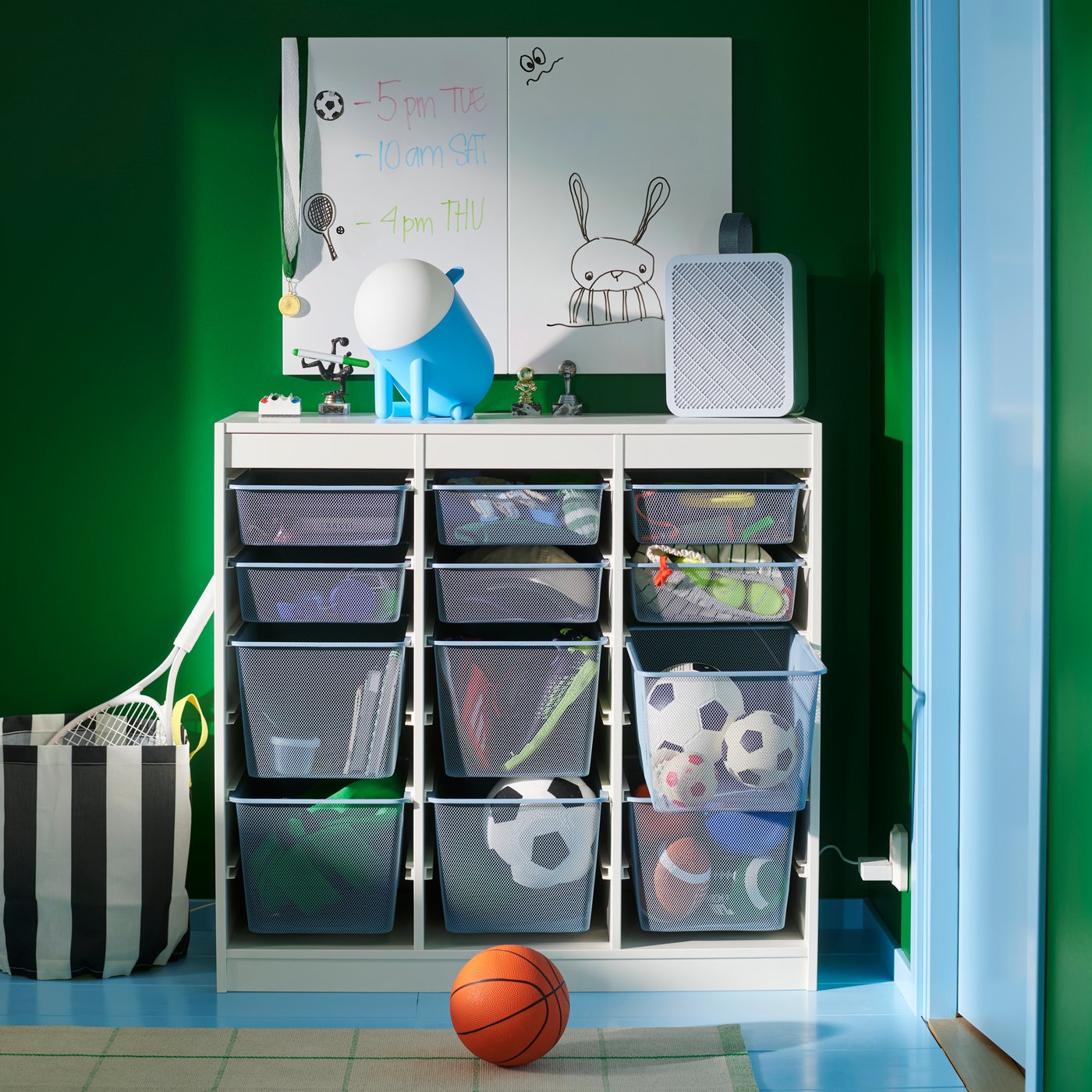 A TROFAST combination with mesh storage boxes storing sports balls and equipment, against a green wall in a children’s room.